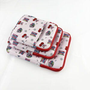 Stack of three different sized neoprene tablet and laptop sleeves featuring cute pink cartoon book and cherry patterns with red zipper closure.